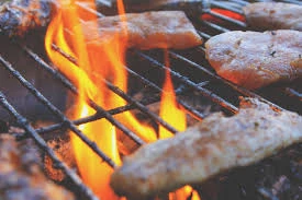 Sausages and meat sizzling on a BBQ grill with flames