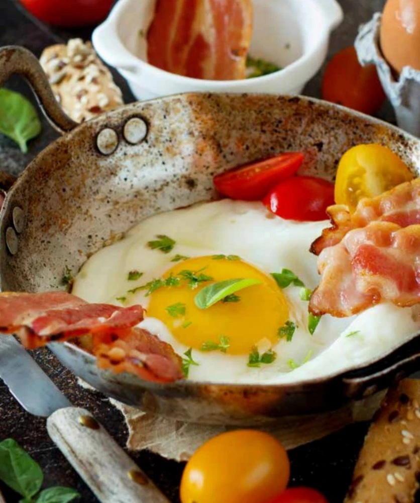 Close-up of fried egg, bacon, and tomatoes in a cast iron pan