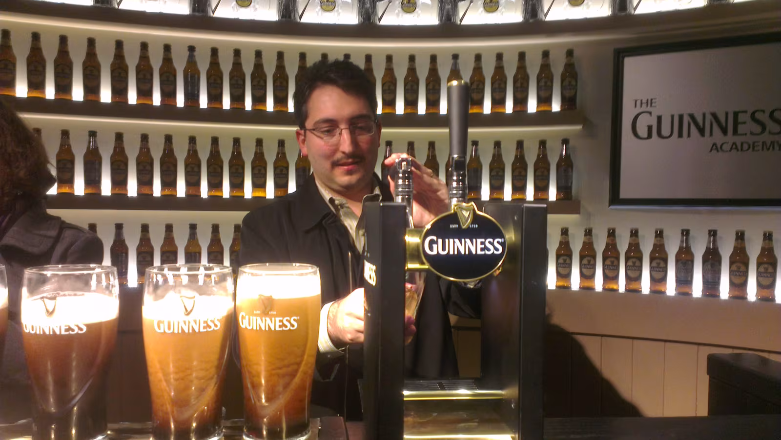A visitor holding up a freshly poured Guinness pint at the perfect pour station inside the Guinness Storehouse, Dublin